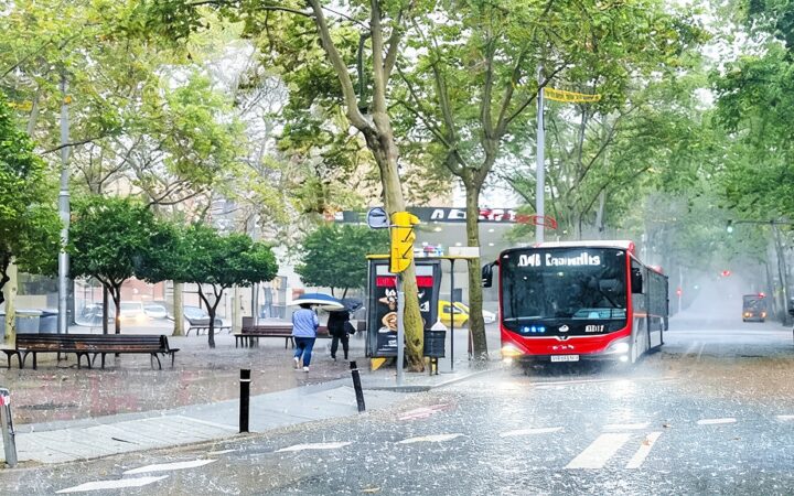Ilustración editorial de un entorno urbano en Cataluña afectado por lluvias intensas y nubosidad tormentosa.